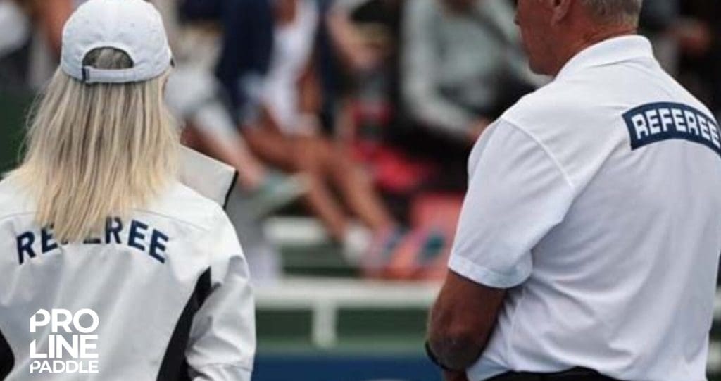 Two pickleball referees observing a match, wearing uniforms labeled ‘REFEREE’—capturing the official side of the game as covered in Pro-Line Paddle’s beginner’s guide to how to play pickleball.